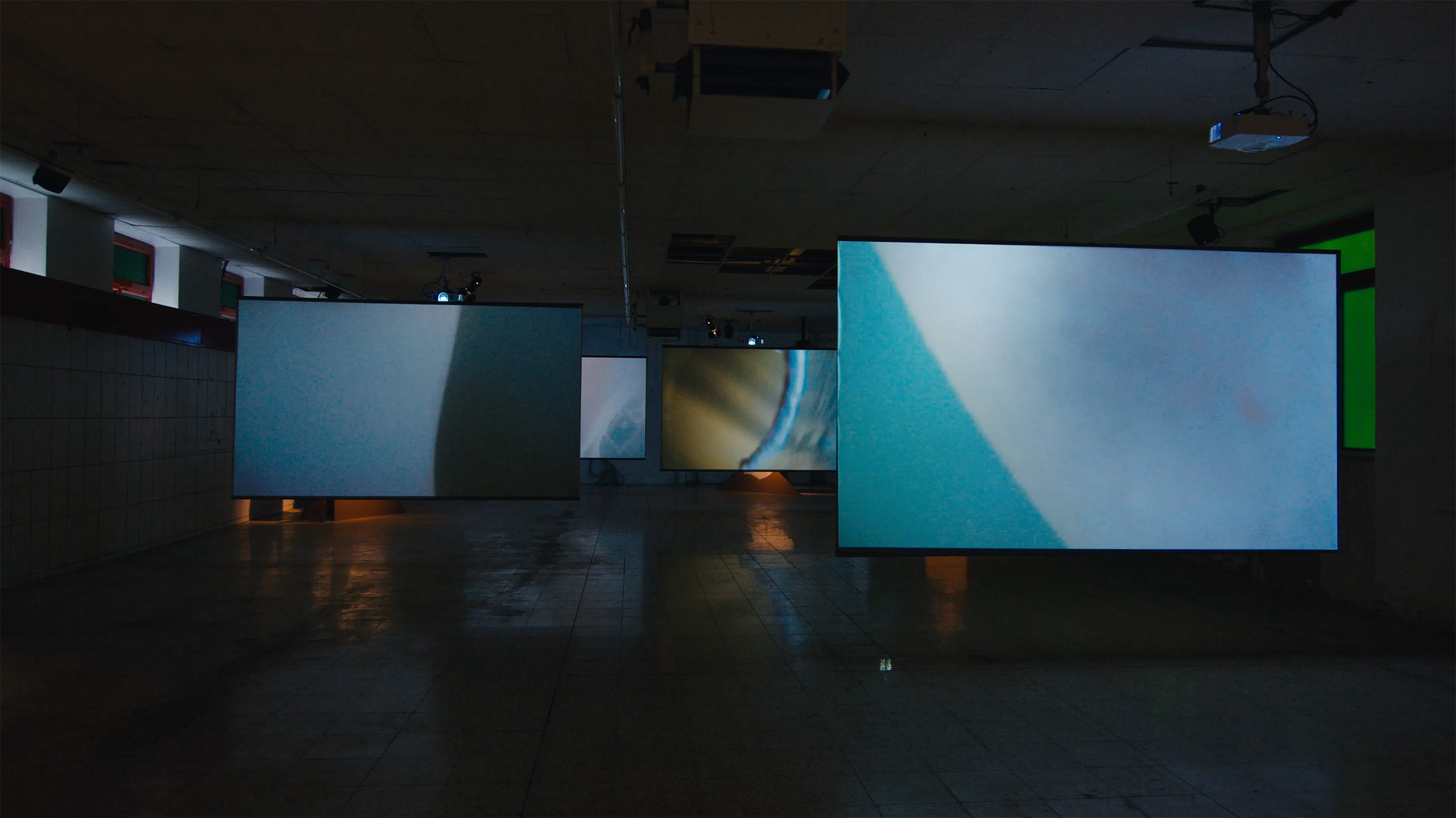 Dark room with four large projection screens hanging, displaying abstract blue and white images.
